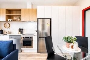 A modern kitchen with stainless steel appliances, a dishwasher, and a dining area with a glass table and black chairs. - Zen Den | Peaceful Retreat Near Wellington (Lower Hutt)