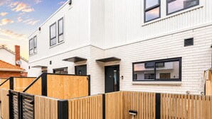 Un edificio residenziale moderno con facciata bianca, infissi neri e recinzione in legno.