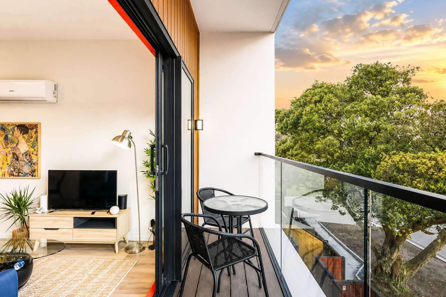 A modern apartment with a balcony, a flat-screen TV, a dining table, and a painting.
