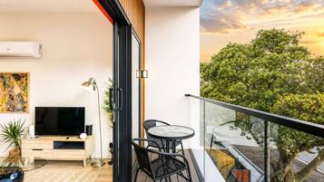 A modern apartment with a balcony, a flat-screen TV, a dining table, and a painting.