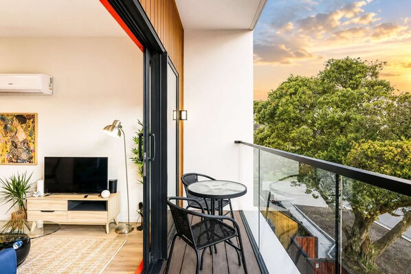 Un apartamento moderno con balcón, televisión de pantalla plana, mesa de comedor y un cuadro.