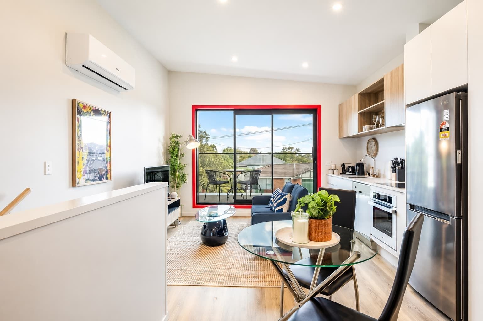 A modern kitchen with a large window, a refrigerator, and a dining area with a glass table.