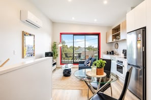 Una cocina moderna con un ventanal grande, un refrigerador y una zona de comedor con una mesa de vidrio.