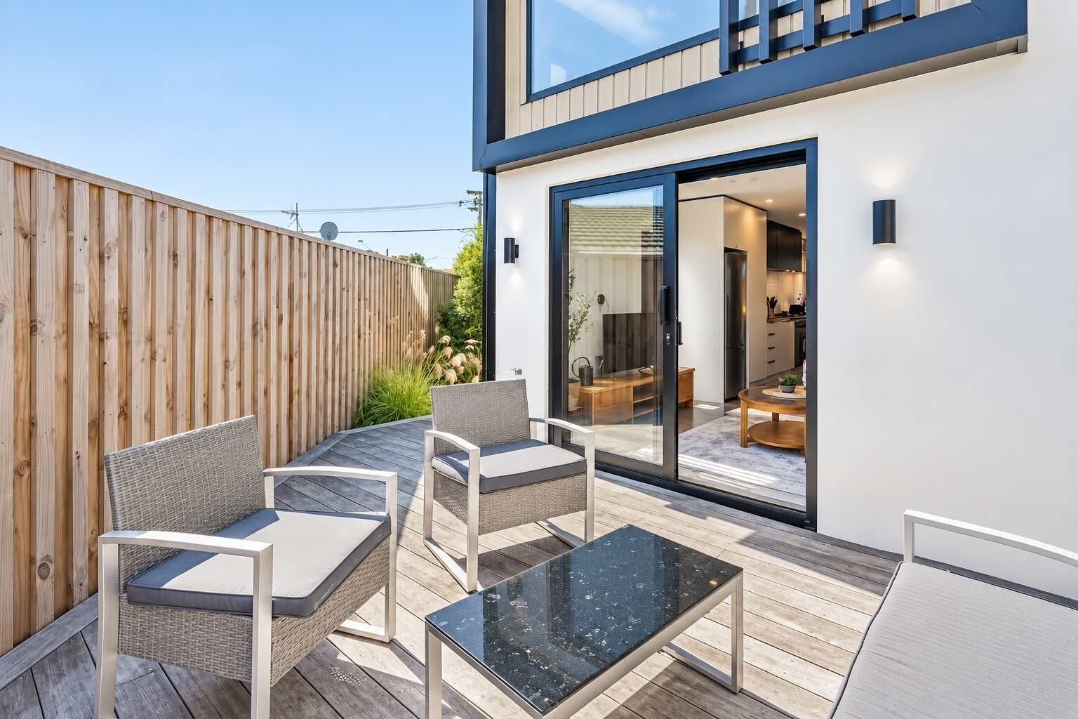 Un patio moderno al aire libre con mobiliario de mimbre, una mesa de vidrio y vista hacia el interior de la casa.