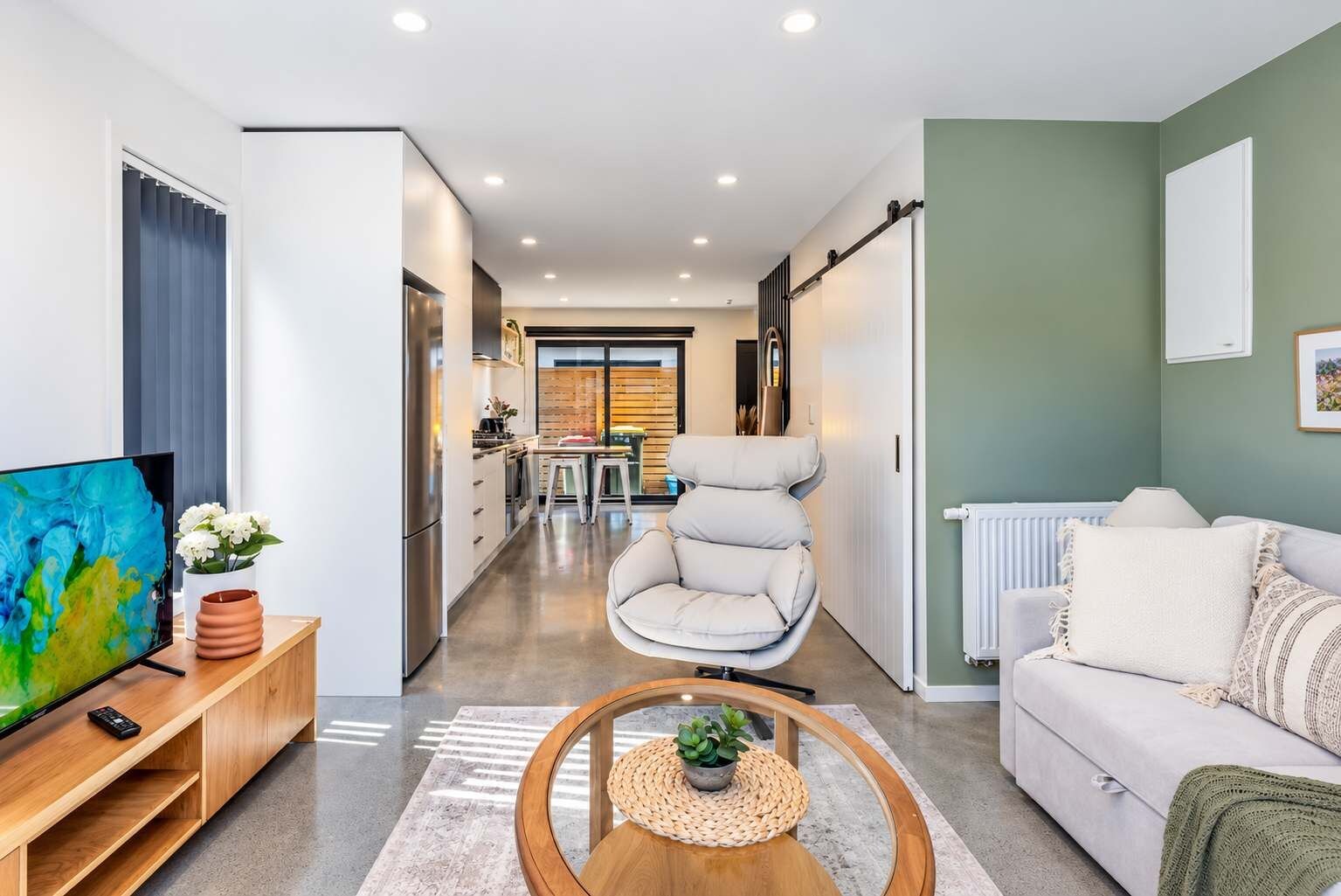 A modern living room with a sofa, a TV, and a dining area with a chair.