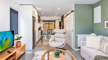 A modern living room with a sofa, a TV, and a dining area with a chair.