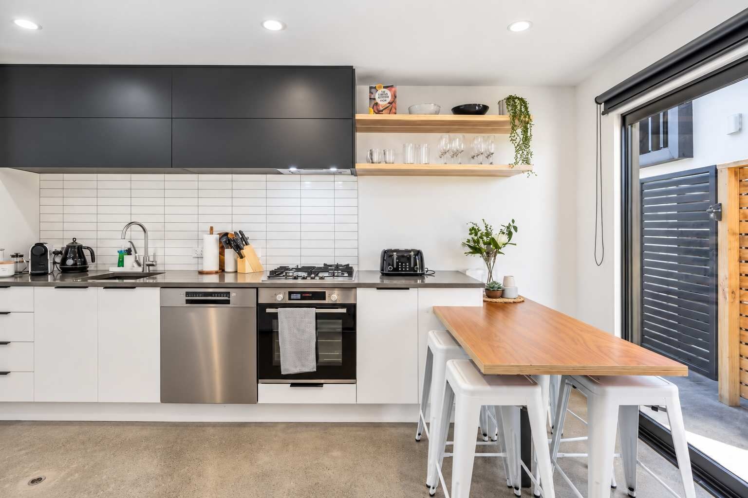 A modern kitchen with white cabinets, stainless steel appliances, a wooden dining table, and a potted plant.