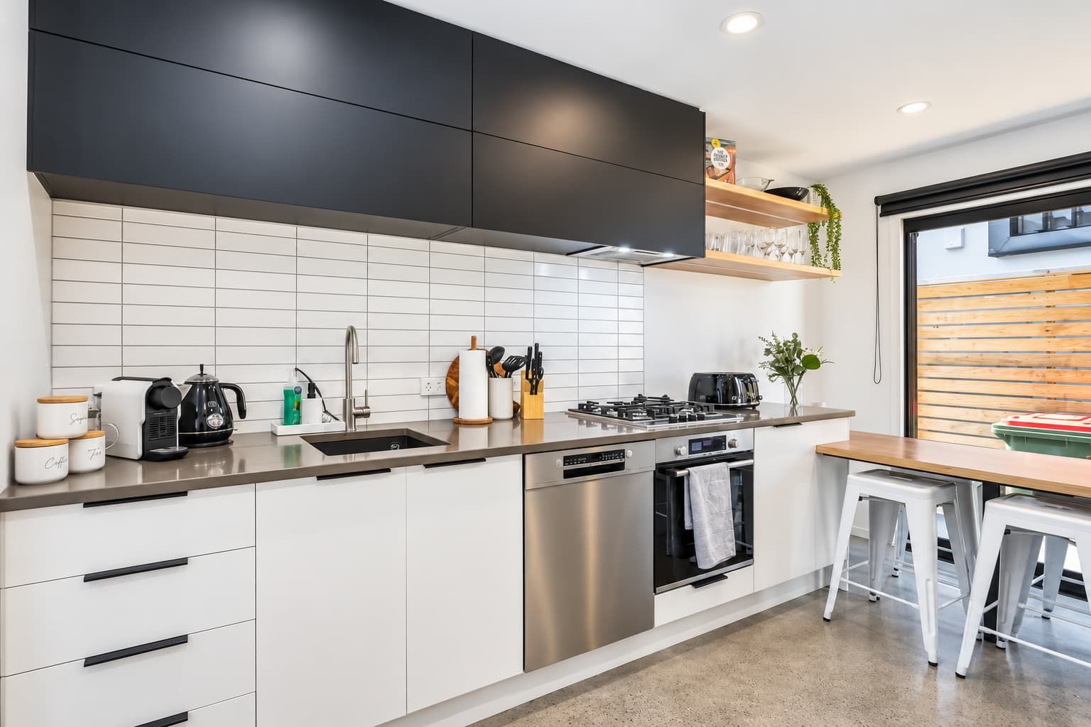 Una cucina moderna con piano cottura in acciaio inossidabile, lavastoviglie e forno integrato. Si vede una finestra con vista all'esterno.