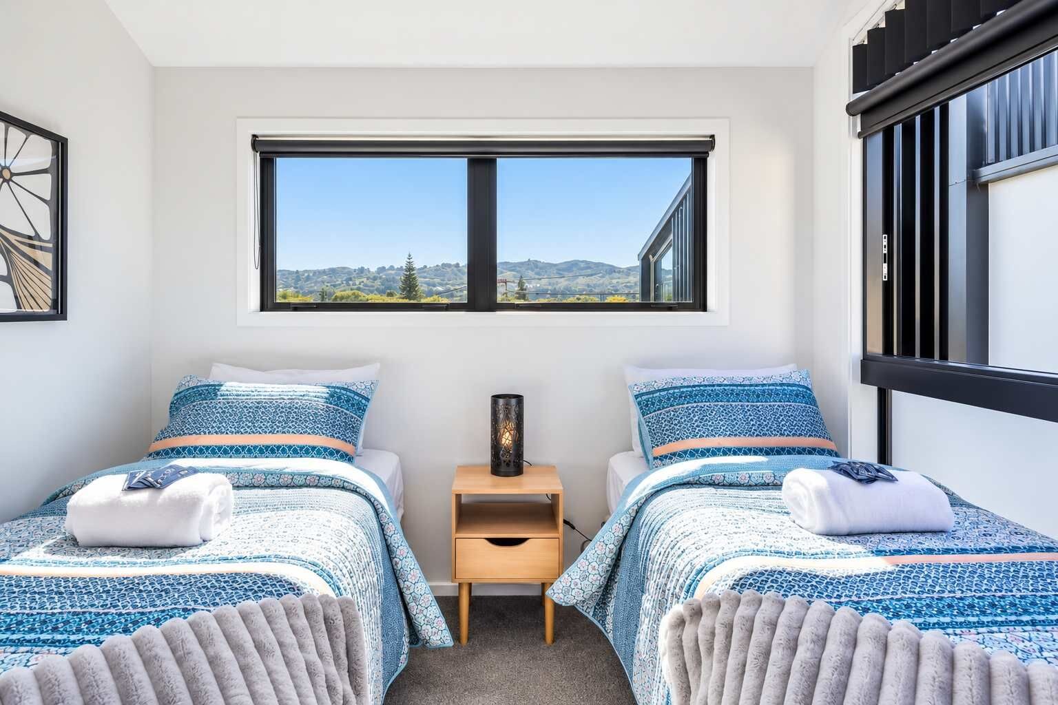 Une chambre avec deux lits, une table de chevet, une fenêtre donnant sur un beau paysage et un tableau encadré au mur.