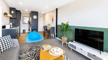 A modern living room with a sofa, a blue chair, a wooden coffee table, a TV, and a dining area with chairs and a table.