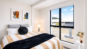 A hotel room with a large window, a bed with striped bedding, a black throw, and two abstract paintings on the wall. - Newtown Tranquility | 2BR Wellington | Kitchen (Wellington)