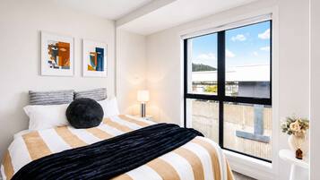 A hotel room with a large window, a bed with striped bedding, a black throw, and two abstract paintings on the wall.