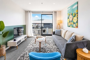 A modern living room with a sofa, a coffee table, a TV, and a balcony with outdoor furniture.