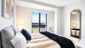 A hotel room with a large bed, a window with a view, a mirror, and a door leading to a balcony.