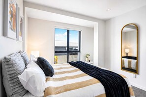 A hotel room with a large bed, a window with a view, a mirror, and a door leading to a balcony.