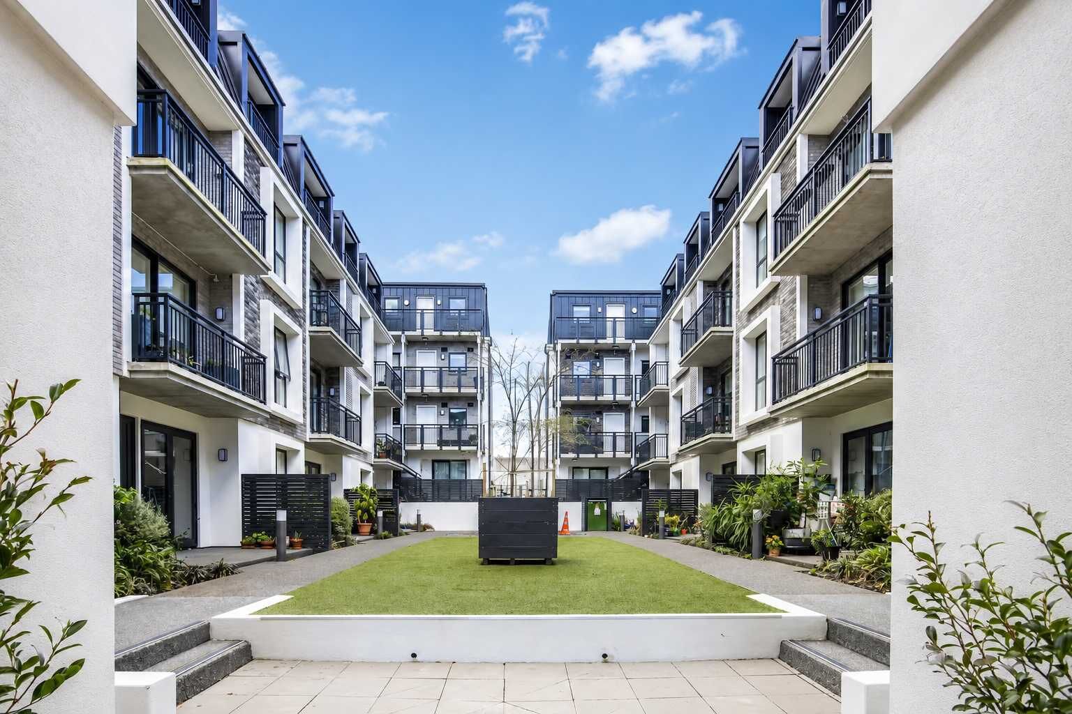 A modern apartment complex with a central courtyard, balconies, and a clear sky.
