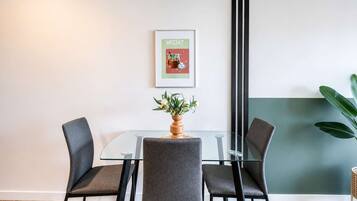 A conference room with a glass table, four grey chairs, a potted plant, and a framed picture on the wall.