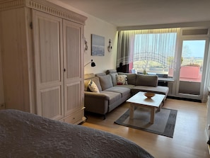 Ein gemütliches Wohnzimmer mit einer Eckcouch, einem kleinen Tisch und einem Kleiderschrank.