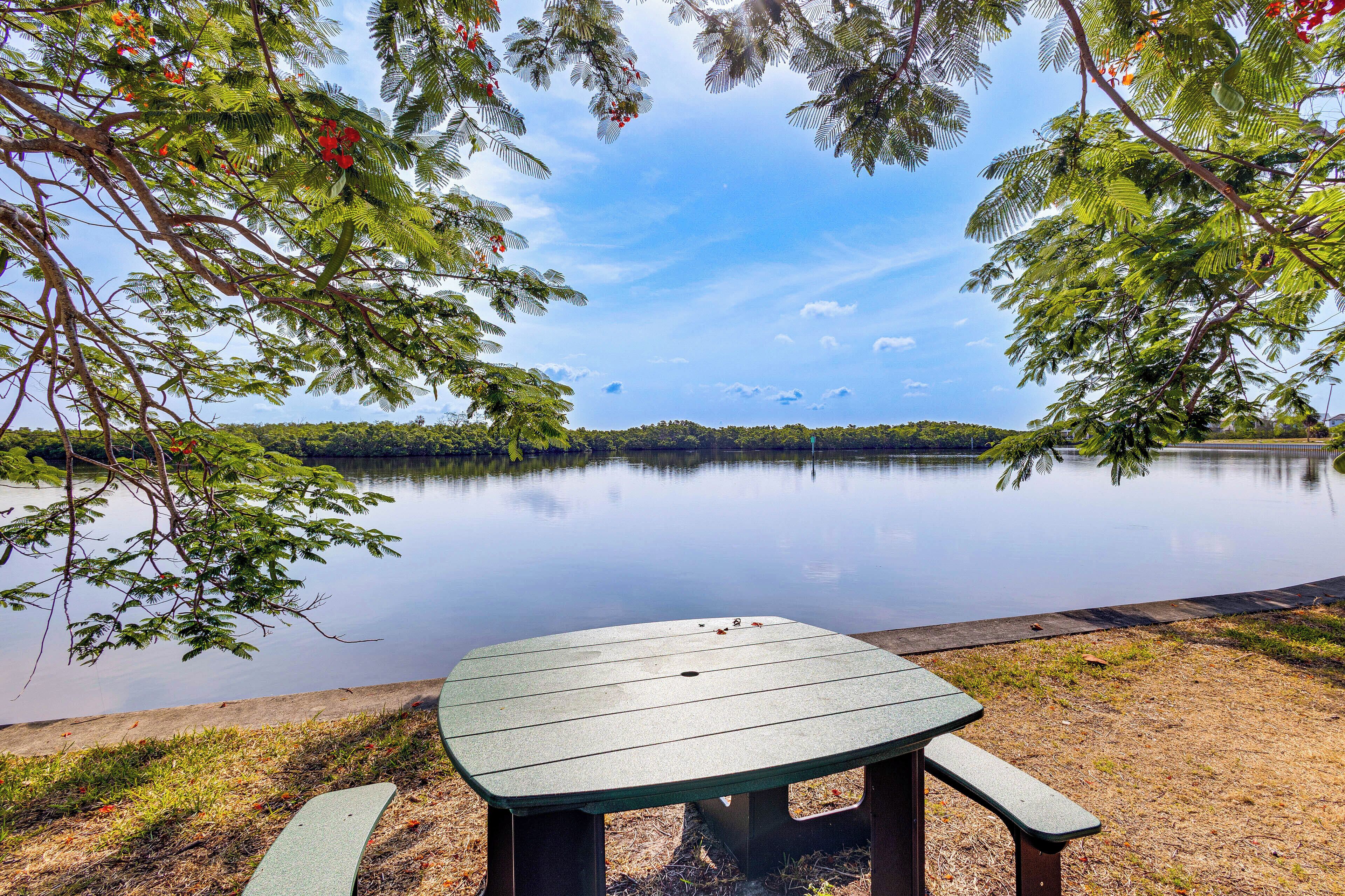 A picnic table by a calm lake with trees in the background.
