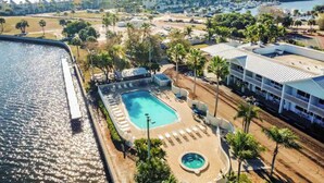 Vue aérienne d’un hôtel avec une piscine, des palmiers et une marina en arrière-plan.