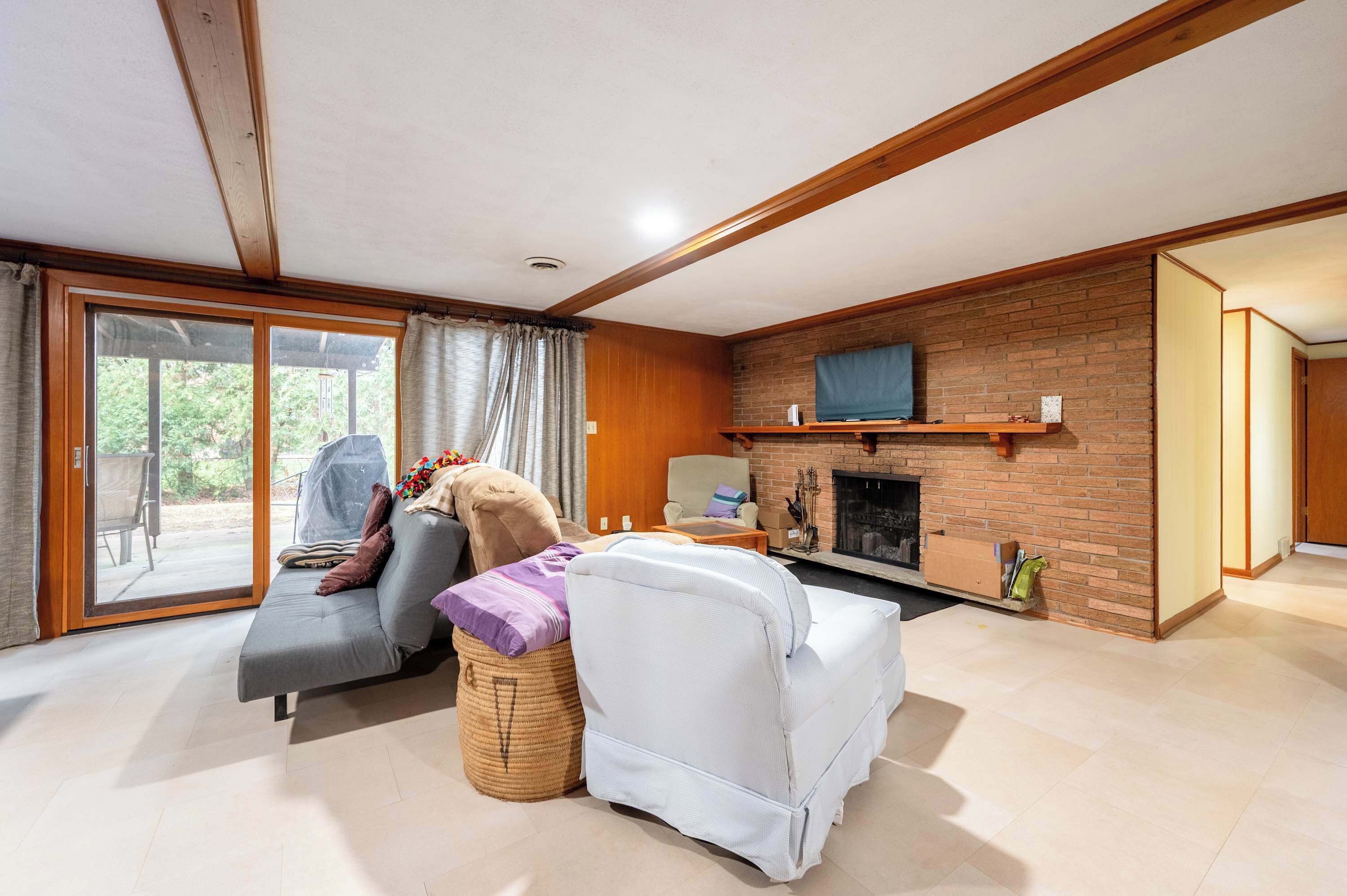 Un salon avec un canapé, un fauteuil et un téléviseur fixé au mur, qui est en briques.