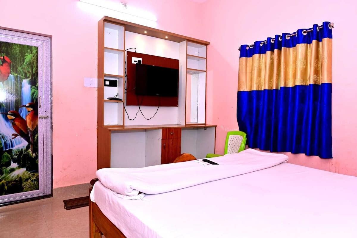 Ein Schlafzimmer mit einem Bett, einem an einer Holzhilfe befestigten Fernseher, einem grünen Sessel und einem Vorhang mit blau-goldenen Mustern.
