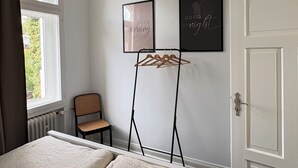 Une chambre avec deux lits, une chaise, un étendoir et deux panneaux encadrés accrochés au mur.