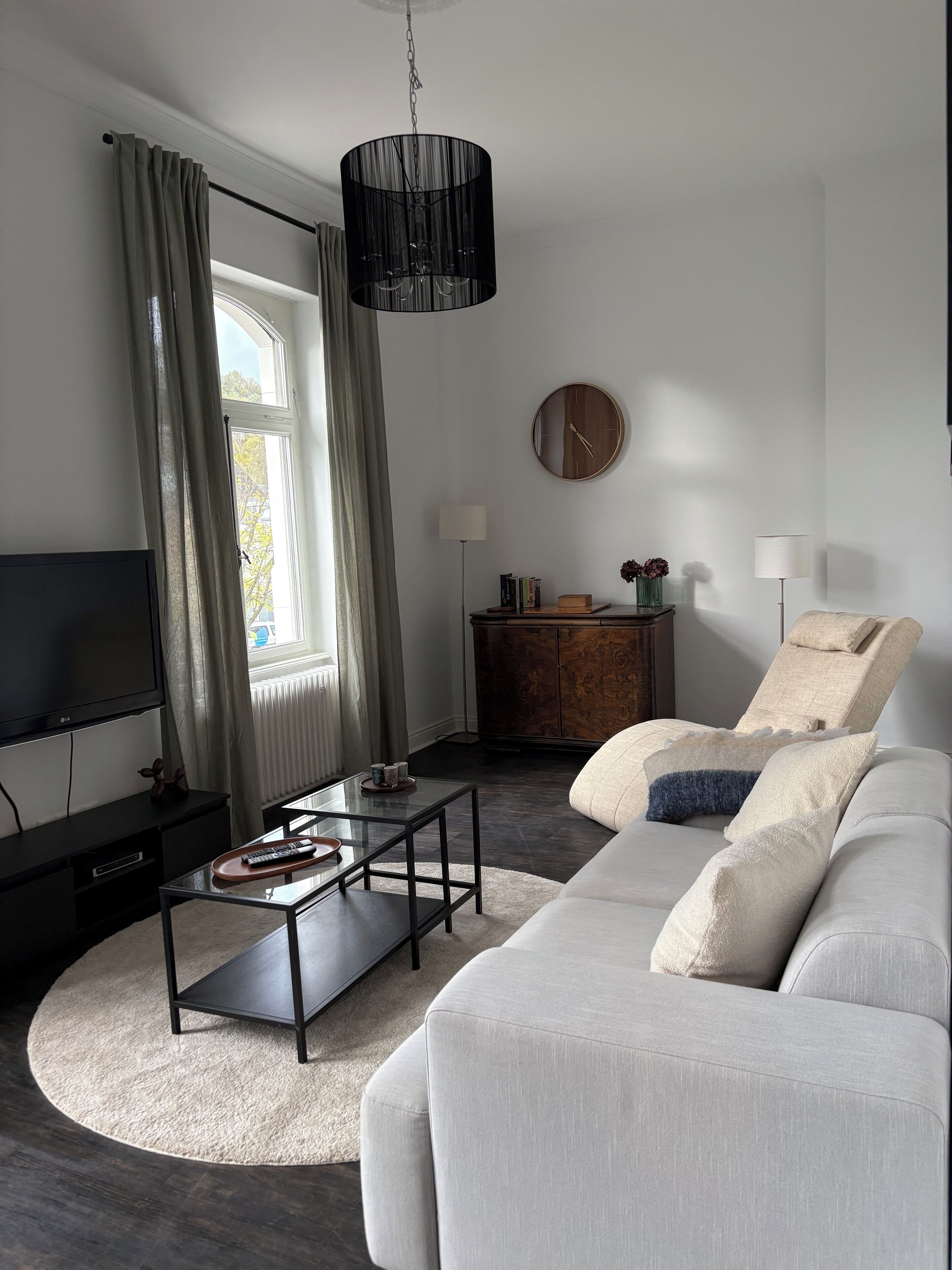 A modern living room with a sofa, a coffee table, a TV, a lamp, and a clock on the wall.