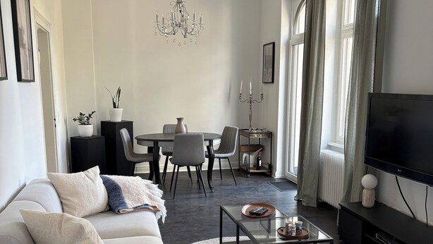 Un salon moderne avec un canapé gris, une table basse en verre et un téléviseur posé sur un meuble noir.