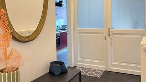 Un couloir avec un grand miroir, une plante en pot, un banc et une porte donnant sur un espace cuisine.