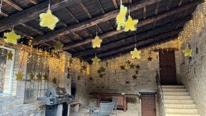 An outdoor patio with stone walls, a wooden ceiling, and string lights. - Uliveto Magico (Cannara)