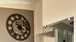A room with a wall-mounted gear clock, a glass shower enclosure, and a white radiator. - Uliveto Magico (Cannara)