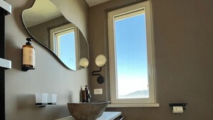 A bathroom with a large mirror, a sink with a bowl, a towel rack, and a window. - Uliveto Magico (Cannara)