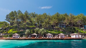 Um resort com bangalôs sobre a água, piscina e vegetação exuberante.