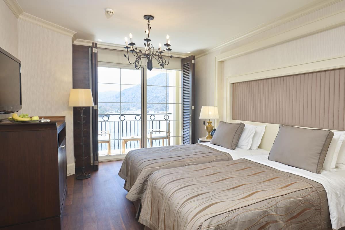 Habitación de hotel con una cama grande, dos mesitas de noche con lámparas, un televisor y un balcón con vistas a las montañas.