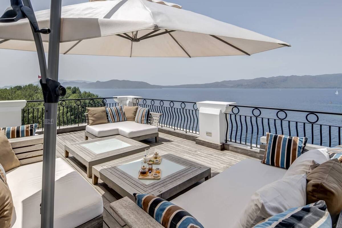 Una terraza con asientos al aire libre, una mesa con bebidas y vistas al mar y las montañas.