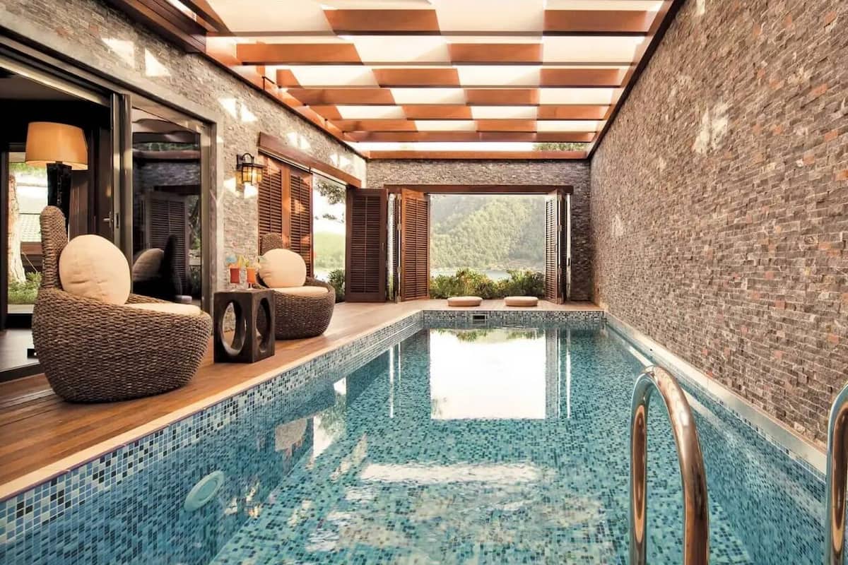 Una piscina interior con suelo de baldosas, cubierta de madera y sillas de mimbre.