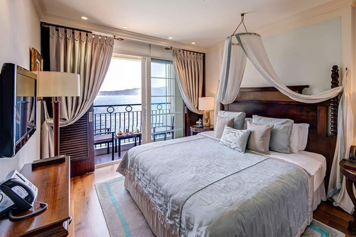 Un dormitorio amplio con una cama grande, un balcón con cortinas, un televisor y una mesita de noche con lámpara.