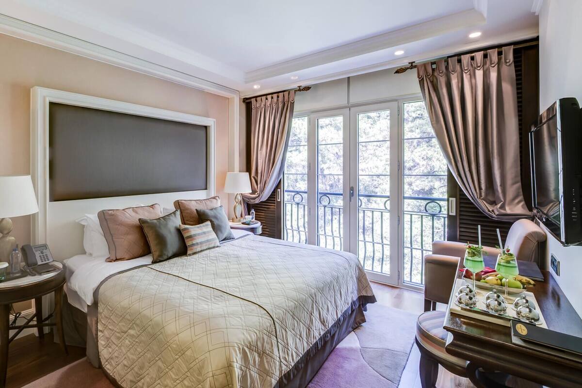 Una habitación de hotel con una cama grande, un escritorio con ordenador, una silla y un balcón con cortinas.
