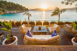 A wooden deck with wicker furniture and planters, overlooking a body of water and a sunset. - Angel's Marmaris Hotel (Marmaris)