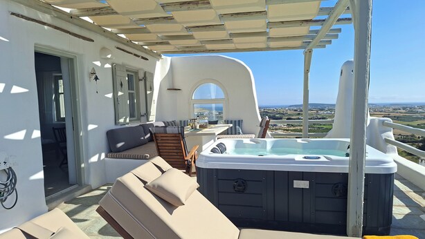 A sunlit outdoor seating area with a hot tub, a cushioned bench, and a view of the landscape. - Studio Eleftheria, Apleton Villas Paros (Paros)