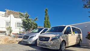 Two parked Mercedes-Benz vans in a driveway with a white building and a tree in the background. - Studio Eleftheria, Apleton Villas Paros (Paros)
