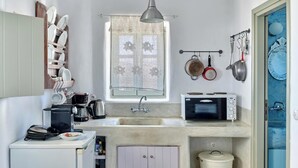 A compact kitchen with a sink, a microwave, and a small refrigerator. There is a window above the sink and a hanging pot rack with pans. - Studio Eleftheria, Apleton Villas Paros (Paros)