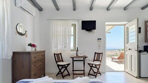 A bedroom with a bed, a desk, two chairs, a dresser, a TV, and a view of the beach. - Studio Eleftheria, Apleton Villas Paros (Paros)