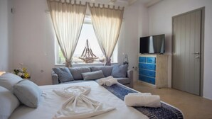 A bedroom with a bed, a television, a wardrobe, and a window with curtains. - Villa Pisti, Apleton Villas Paros (Paros)