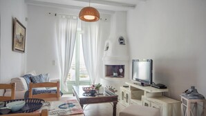 Ett vardagsrum med en soffa, ett soffbord, en tv på ett tv-bord och ett fönster med gardiner.