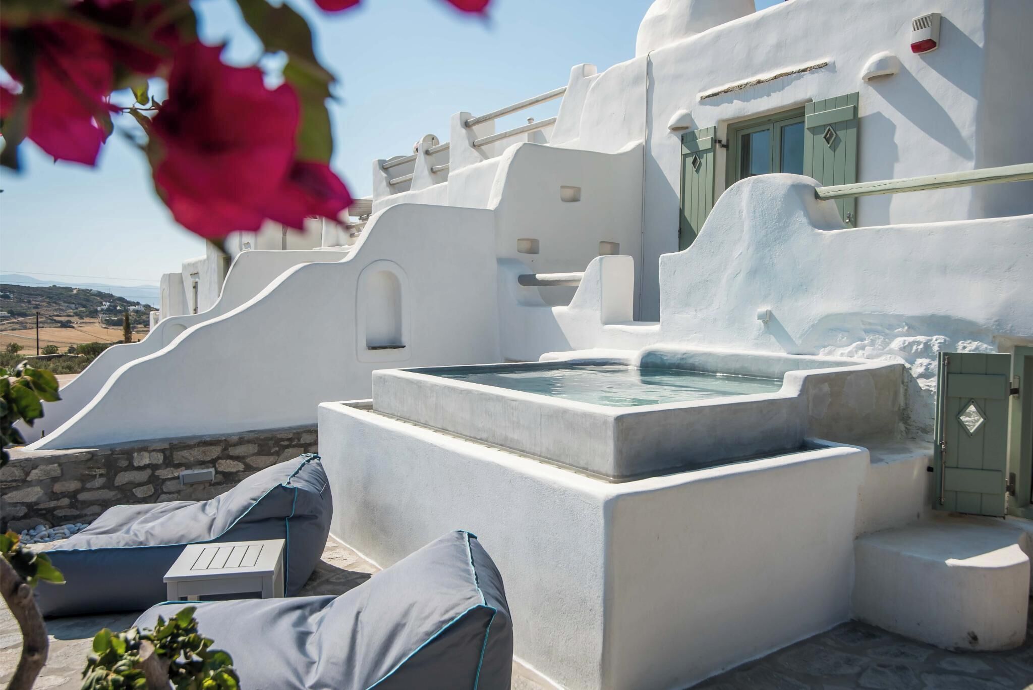 Un bâtiment blanc avec un mur en pierre et un jacuzzi. On y trouve deux chaises longues et une petite table.
