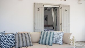 Un divano beige con cuscini decorati, una porta bianca con aperture a rombo e una ventola a soffitto.
