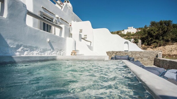 Un edificio bianco con piscina, mura in pietra e cielo azzurro intenso.