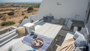 Una terrazza sul tetto con una zona salotto esterna bianca, un tavolo con tovaglia fantasia e vista sulla campagna.
